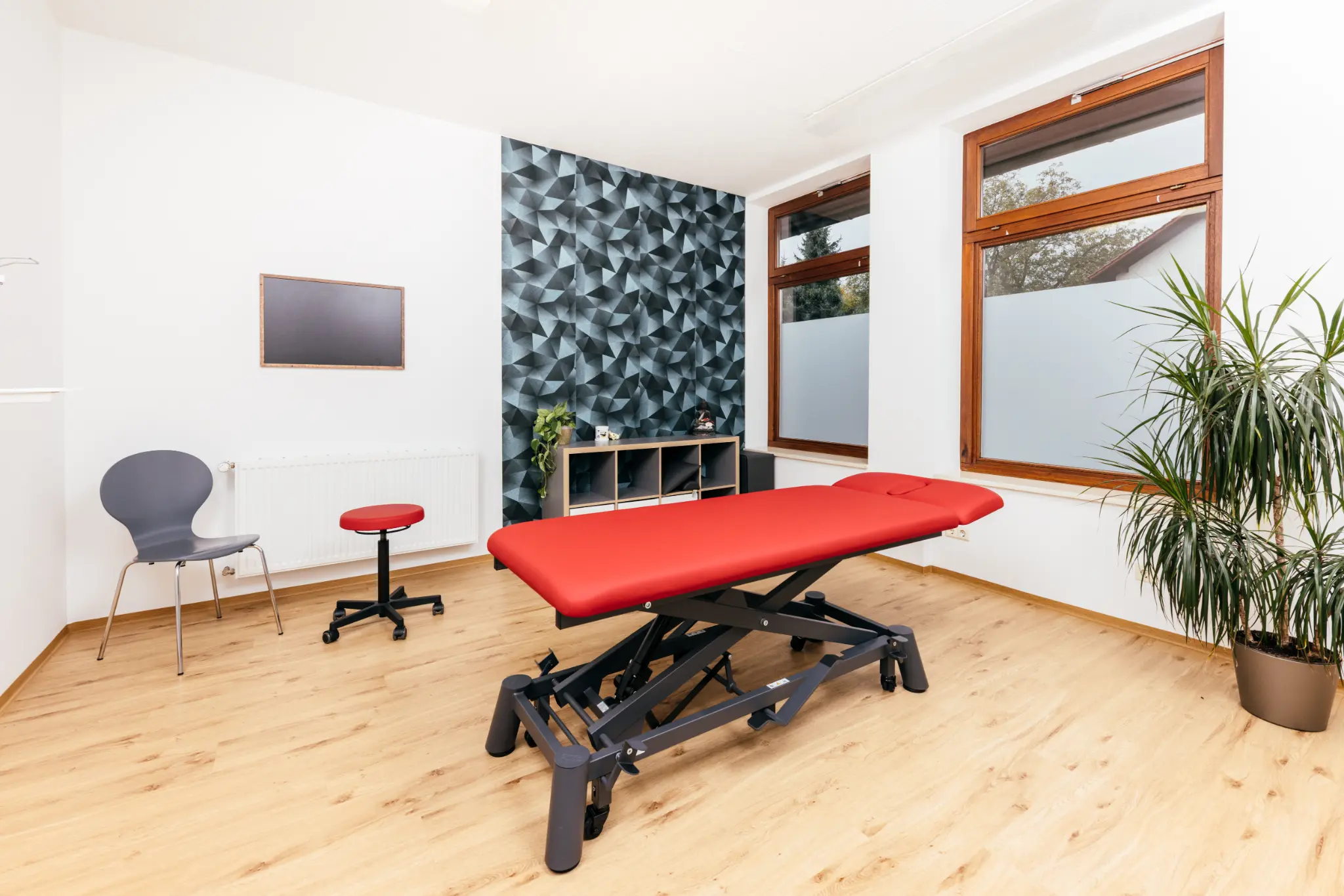 Heller Behandlungsraum mit roter Therapieliege