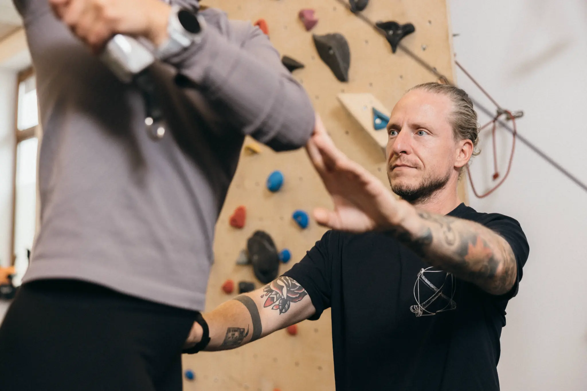Therapeut zeigt eine Übung mit Kletterwand im Hintergrund